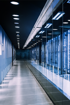 A modern data center corridor with rows of illuminated server racks behind glass walls, blue LED lights highlighting the equipment. The polished floor and ceiling lights create a futuristic, high-tech atmosphere. No people are present.
