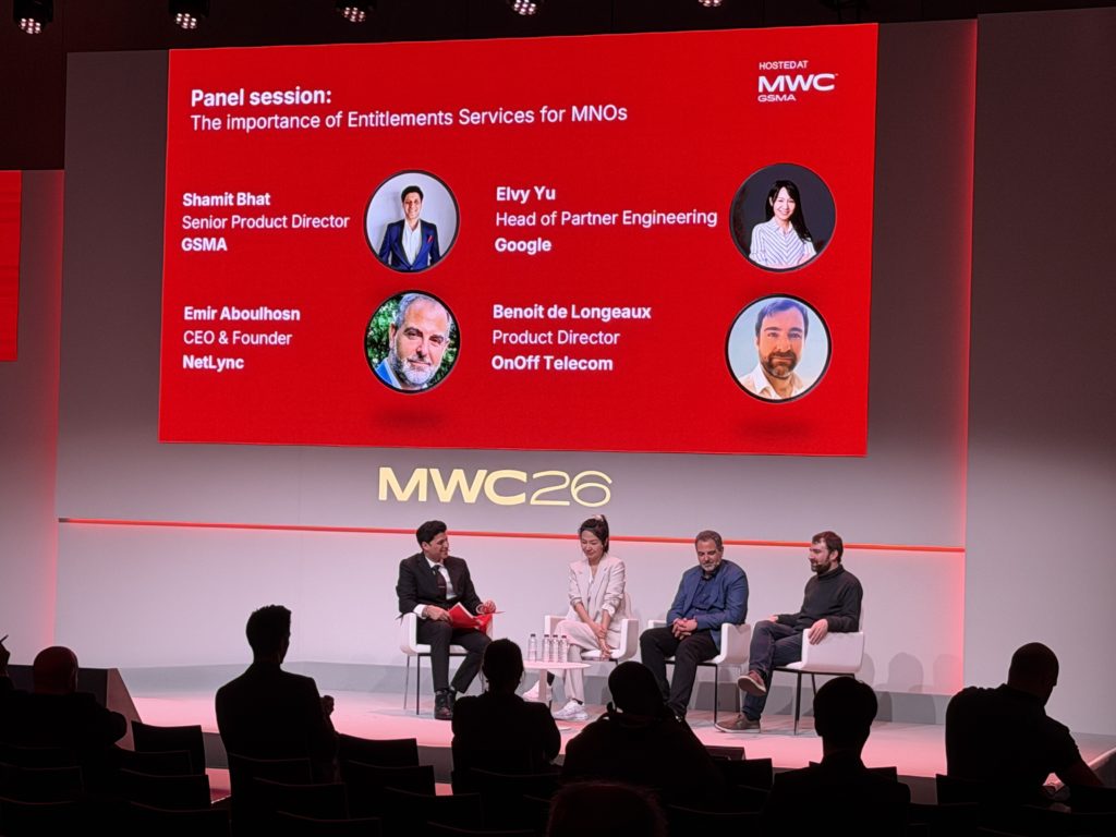 Four panelists sit on stage at MWC 26, discussing MNO entitlements. Behind them, a red screen displays their names, roles, and companies: Shanit Bhat, Elvy Yu, Emir Aboulhosn, and Benoît de Longueaux. Audience members sit facing the stage.