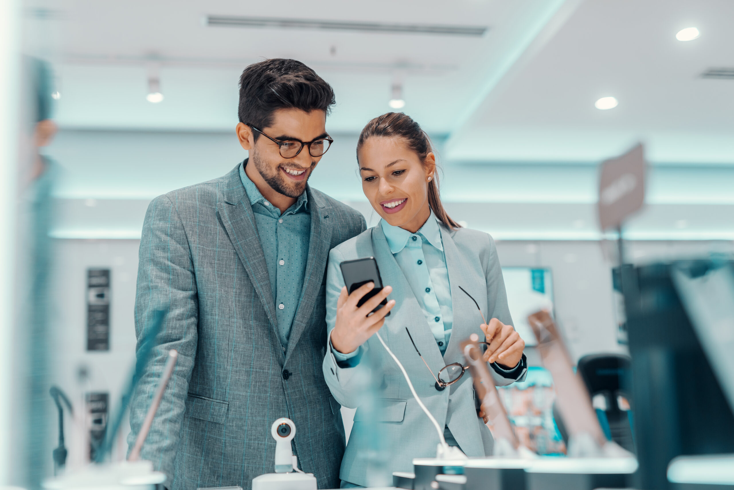 Smiling multicultural couple dressed elegant choosing new smart phone while standing in tech store.